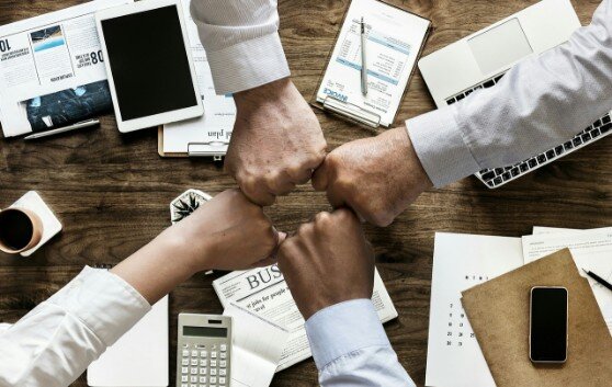 Teamgeist bekräftigen Auf diesem Foto sehen Sie 4 Fäuste über einem Schreibtisch, welche den Teamgeist symbolisieren